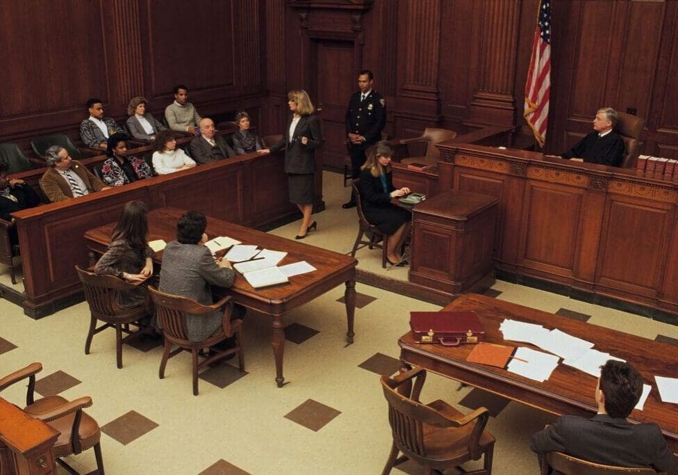 A courtroom with judges and defendants in the foreground.