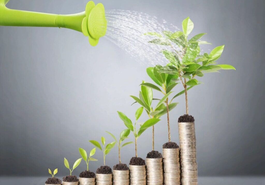 A watering can spraying water on plants growing from stacks of coins.